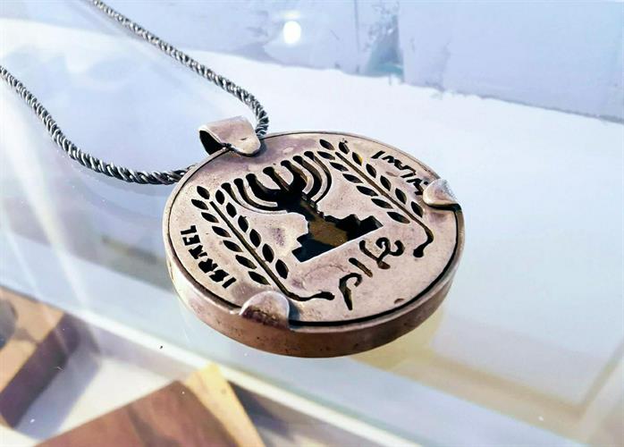 מטבע העצמה, To Be מאת ציפורה אוריה,  תליון כסף בהשראת סמל המנורה עם שני ענפי זית בתוספת המילה שלום, לקוח ממטבע חצי לירה ישראלית ישנה