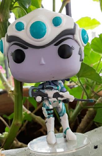 בובת פופ של הדמות ווידו מייקר, Widow Maker,  ממשחק המחשב Overwatch, ממוספרת וחתומה ניצבת על מתקן העמדה שקוף